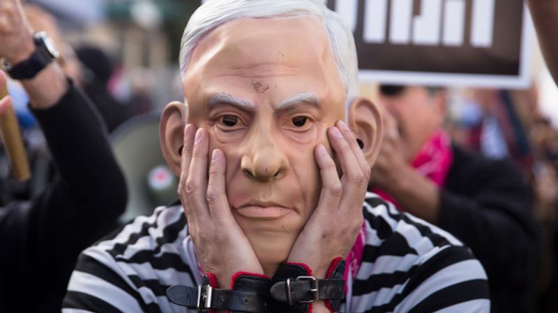 متظاهر يرتدي قناعًا لوجه رئيس الوزراء الإسرائيلي السابق في أثناء جلسة للمحكمة المركزية للنظر في اتهام نتنياهو  بالكسب غير المشروع، في أبريل الماضي (غيتي)