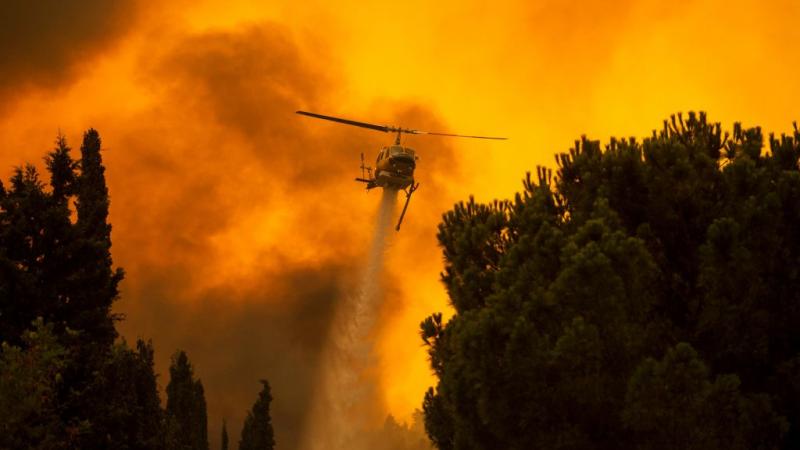 طائرة هليكوبتر تعمل على إخماد الحريق الهائل بقرية فيلا، شمال غرب أثينا (غيتي)