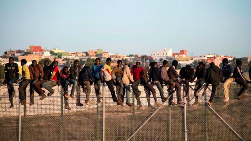 مهاجرون أفارقة يقفون فوق سياج حدودي يفصل المغرب عن جيب مليلية الإسباني 