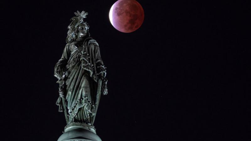 القمر كما بدا خلال الخسوف فوق تمثال الحرية لمبنى الكابيتول في واشنطن (غيتي)