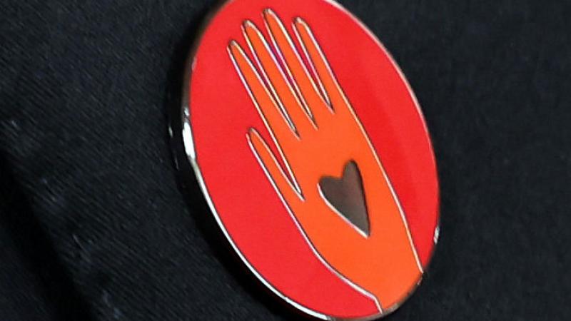 يرمز دبوس اليد الحمراء إلى الحاجة الملحة للدعوة لإنقاذ الأرواح ووقف إطلاق النار في غزة، ويتوسطه قلب في دعوة للانقياد إلى الحب